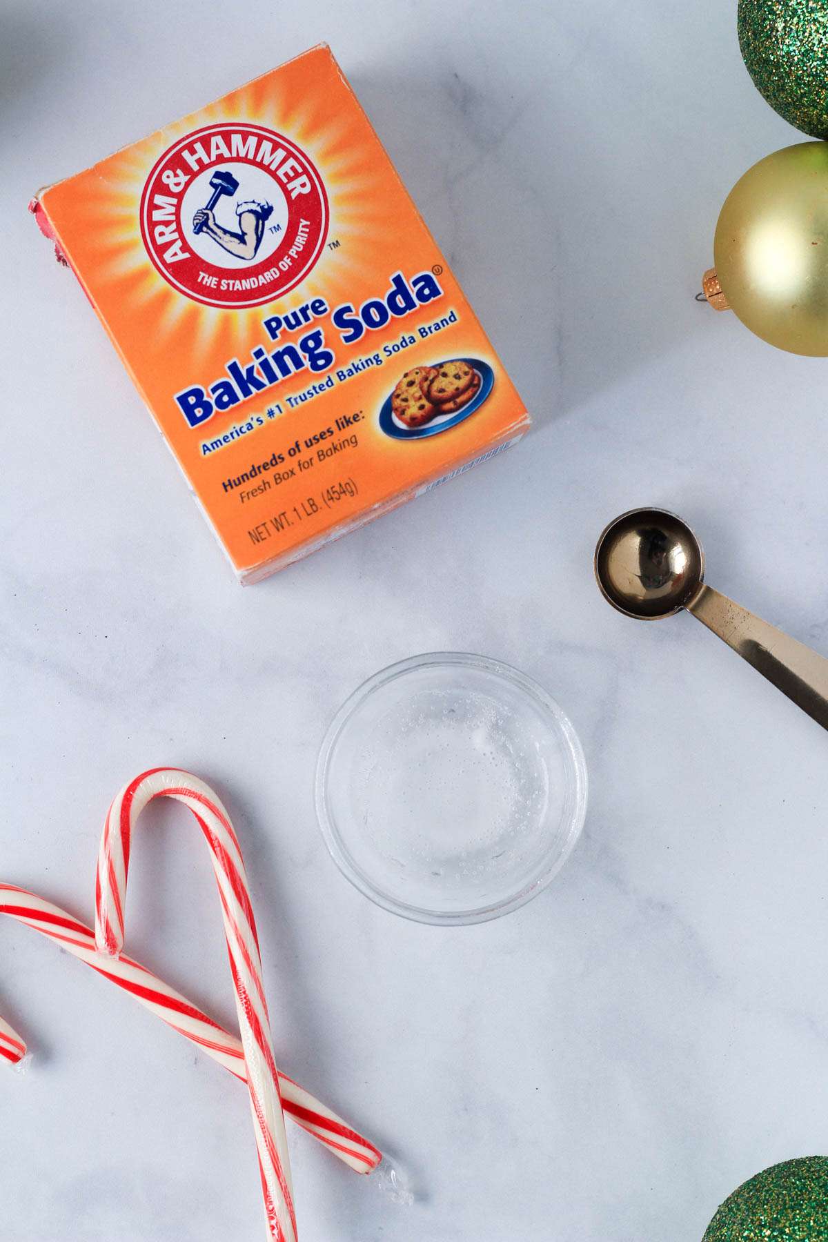 Baking soda in a small glass bowl with a measuring spoon to the right and a few candy canes to the left.