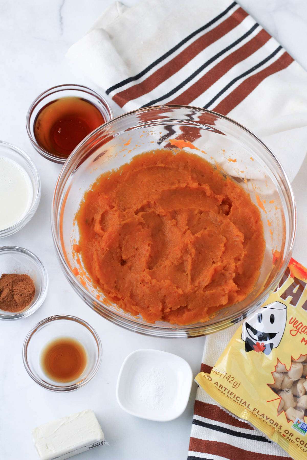 Ingredients for vegan maple sweet potato casserole on a white counter with a brown and cream dish towel and Dandies Maple Marshmallows to the right.