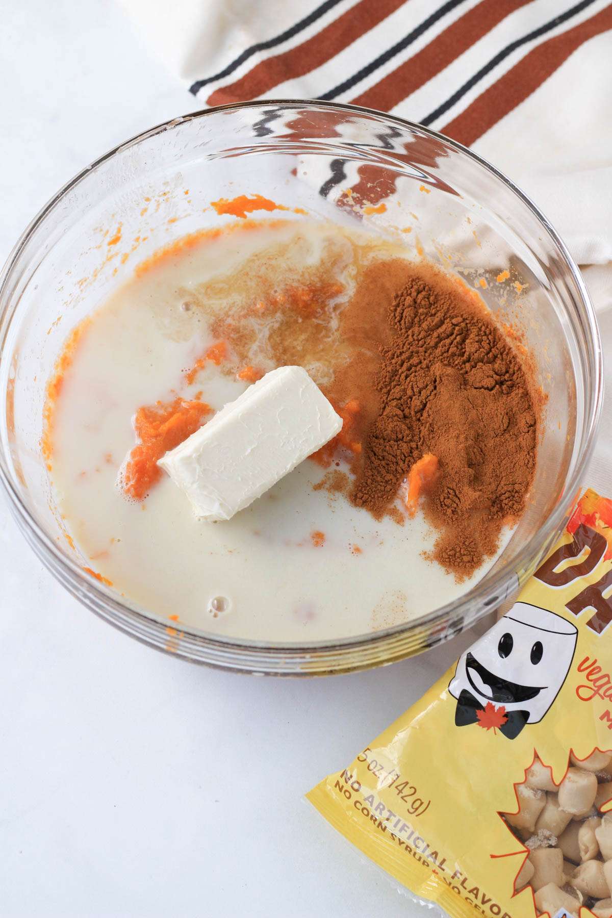 A glass bowl with the ingredients for sweet potato casserole before blending together and a bag of Dandies Vegan Maple Marshmallows to the right.