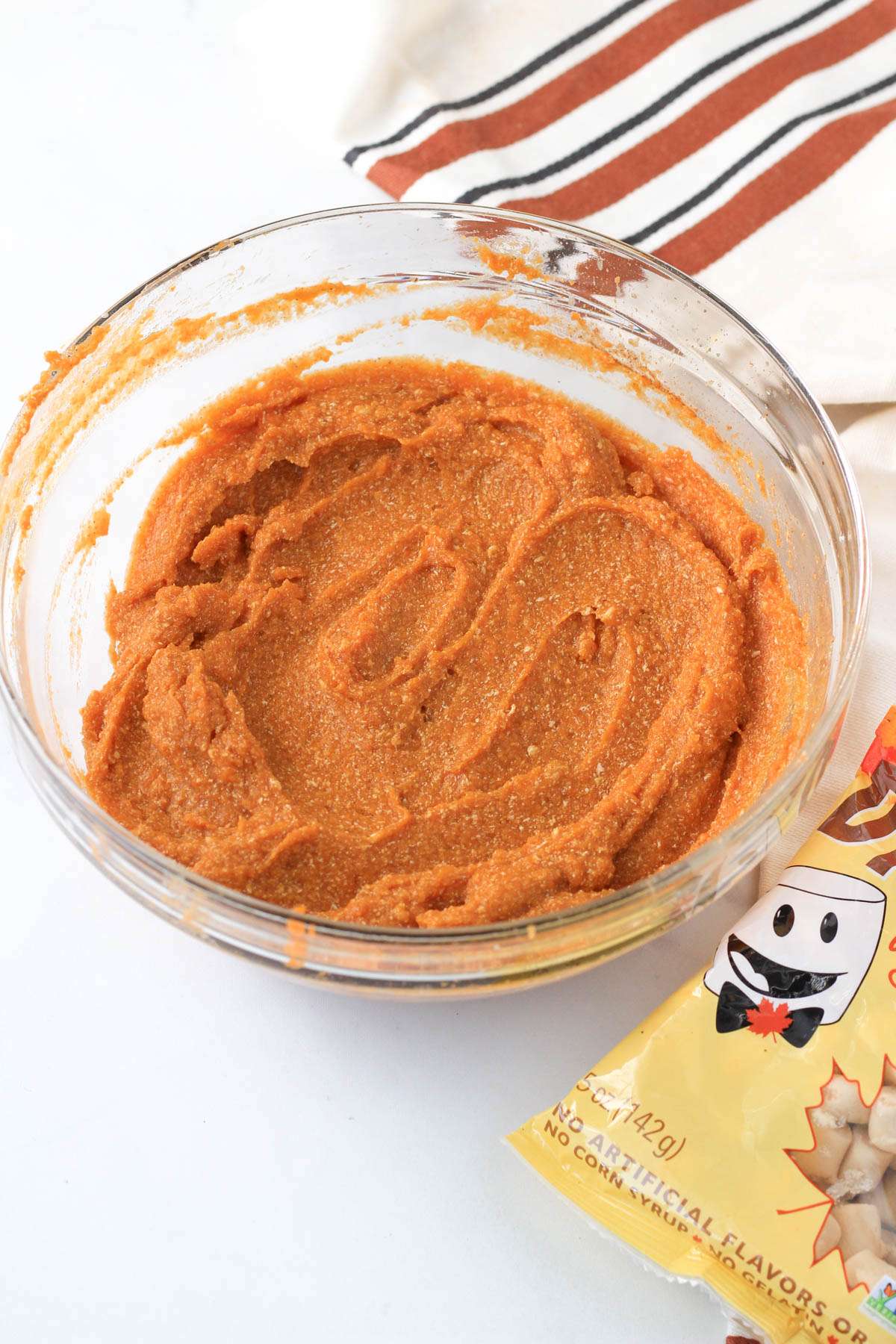 A glass bowl with maple sweet potato casserole after blending with a bag of Dandies vegan maple marshmallows to the right.