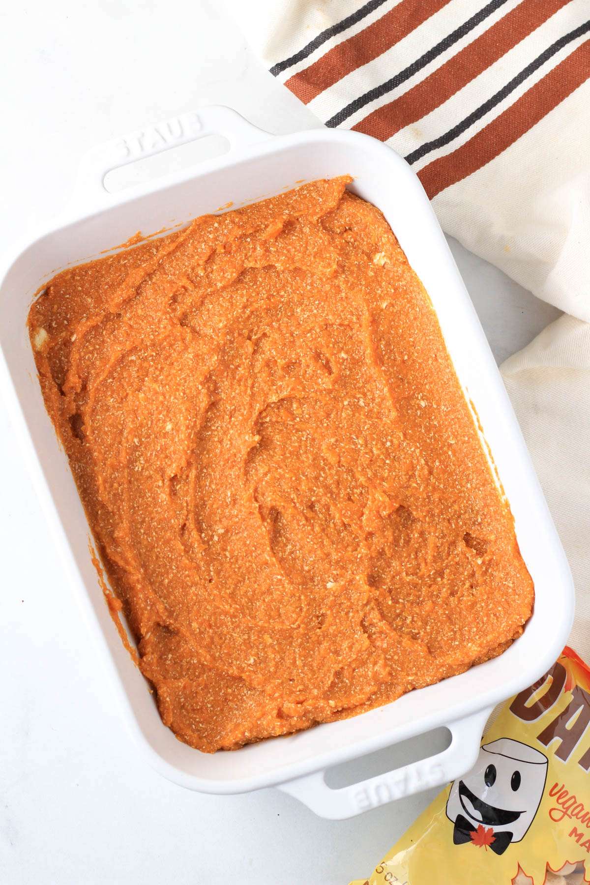A white baking dish with maple sweet potato casserole before baking and a bag of maple marshmallows to the right.