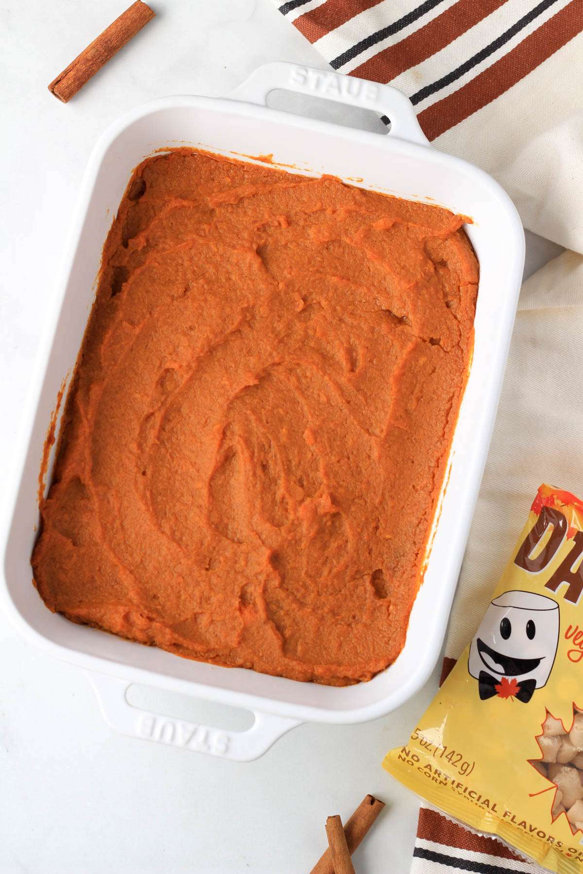 Vegan maple sweet potato casserole in a white dish after baking with a bag of dandies maple marshmallows to the bottom right.