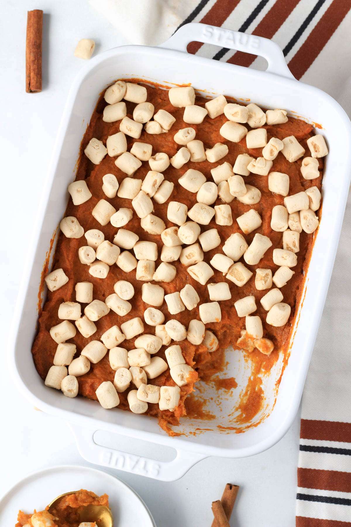 A top down photo of a white baking dish with maple sweet potato casserole topped with dandies marshmallows and a scoop taken out.