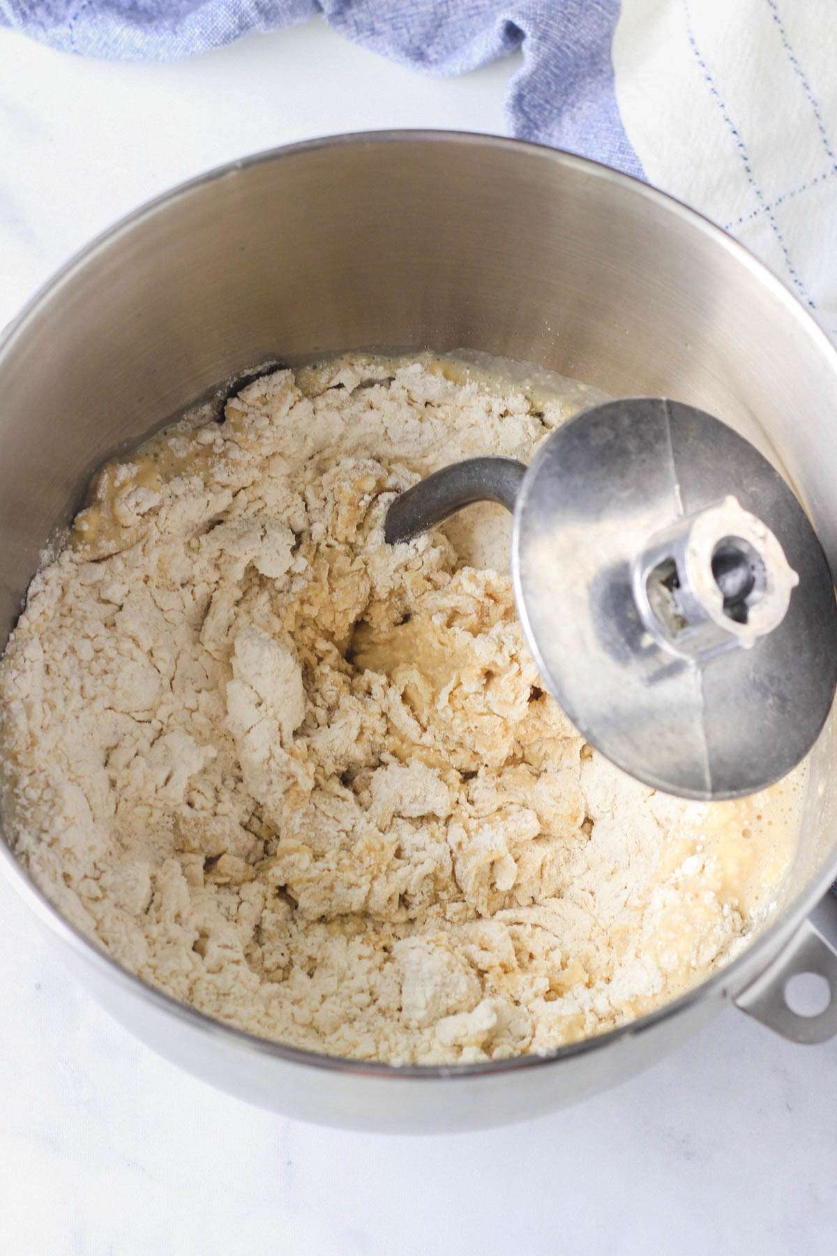 A silver mixing bowl with the ingredients for the vegan dinner roll dough before being kneaded into a ball.
