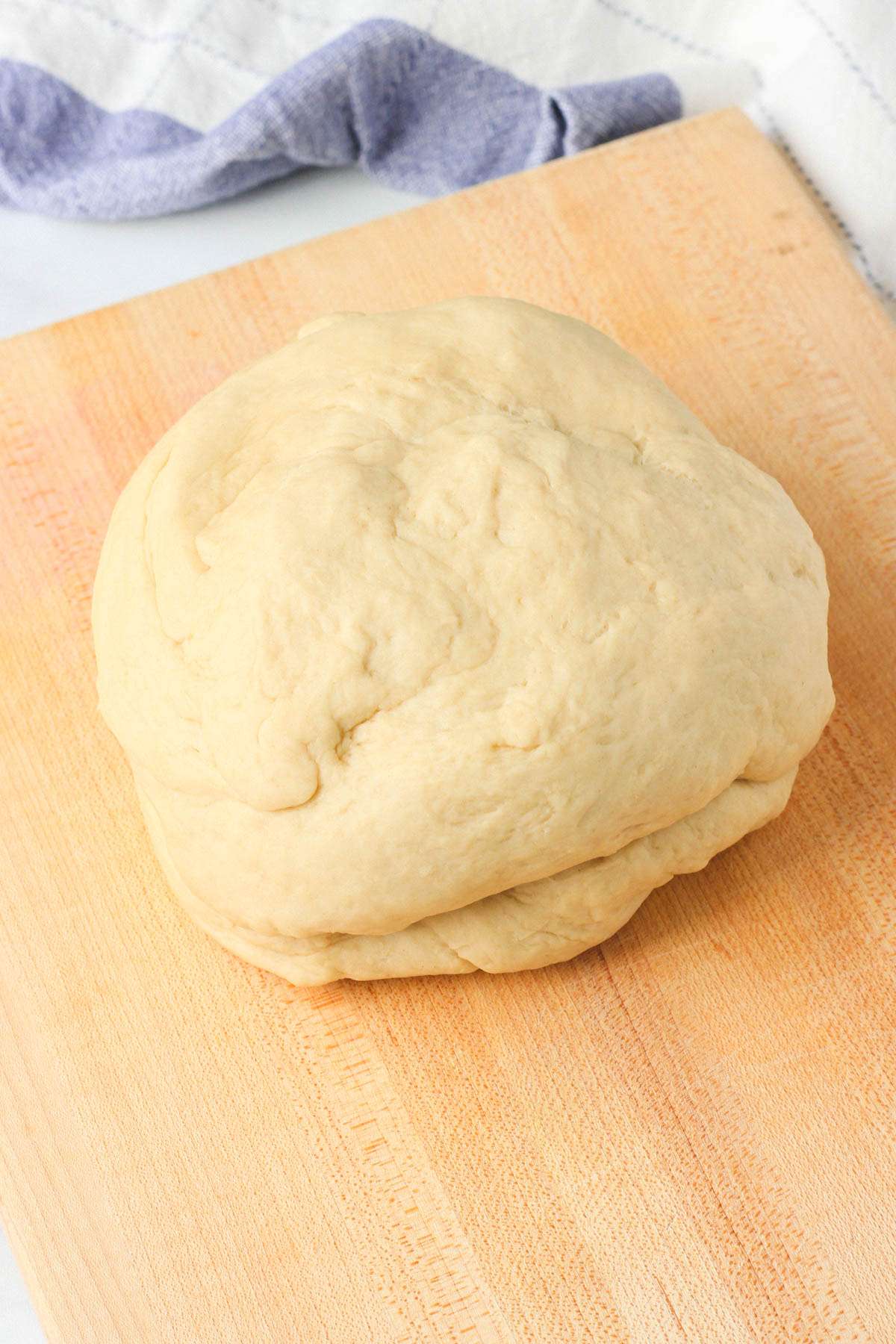 A ball of kneaded vegan dinner roll dough on a wooden counter before being divided into balls.