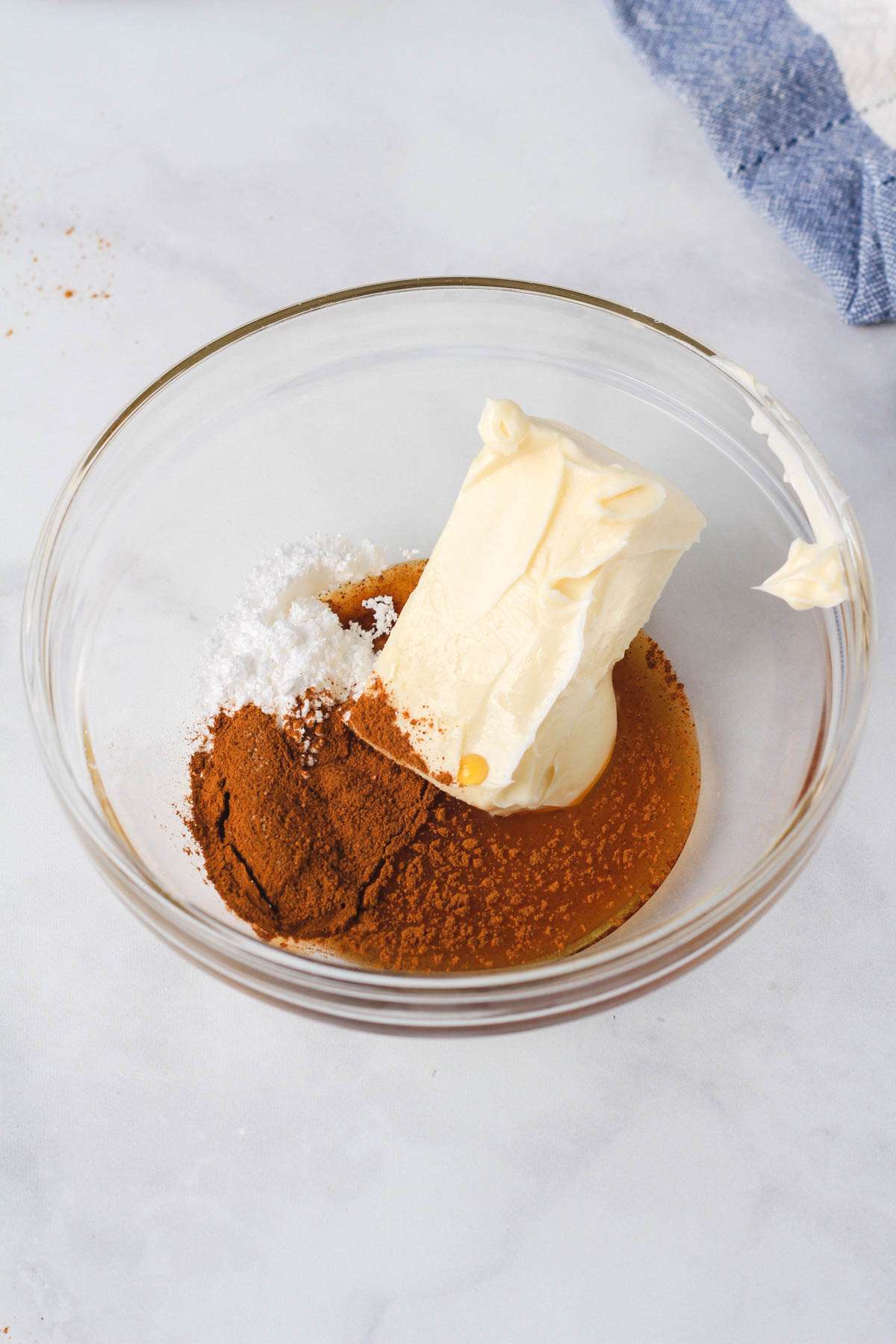 A small glass bowl with unmixed ingredients for cinnamon maple butter on a white counter.