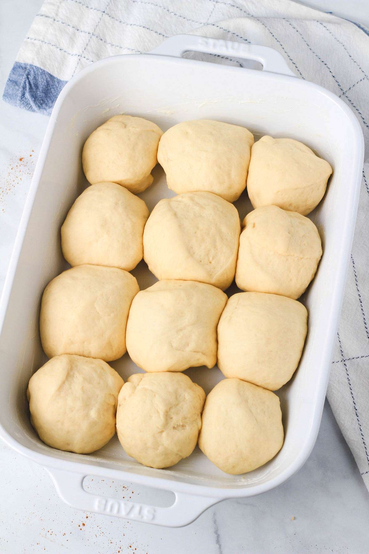 A white baking dish with vegan dinner rolls after resting but before baking.