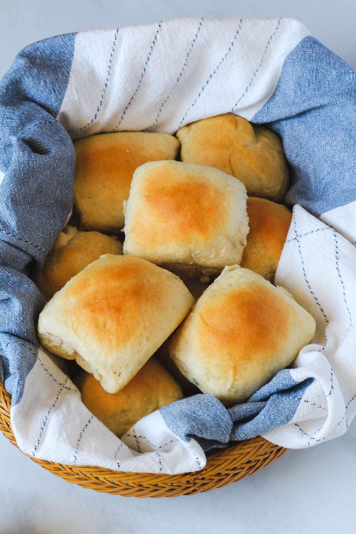 A brown basket with a white and blue towel topped with vegan dinner rolls.