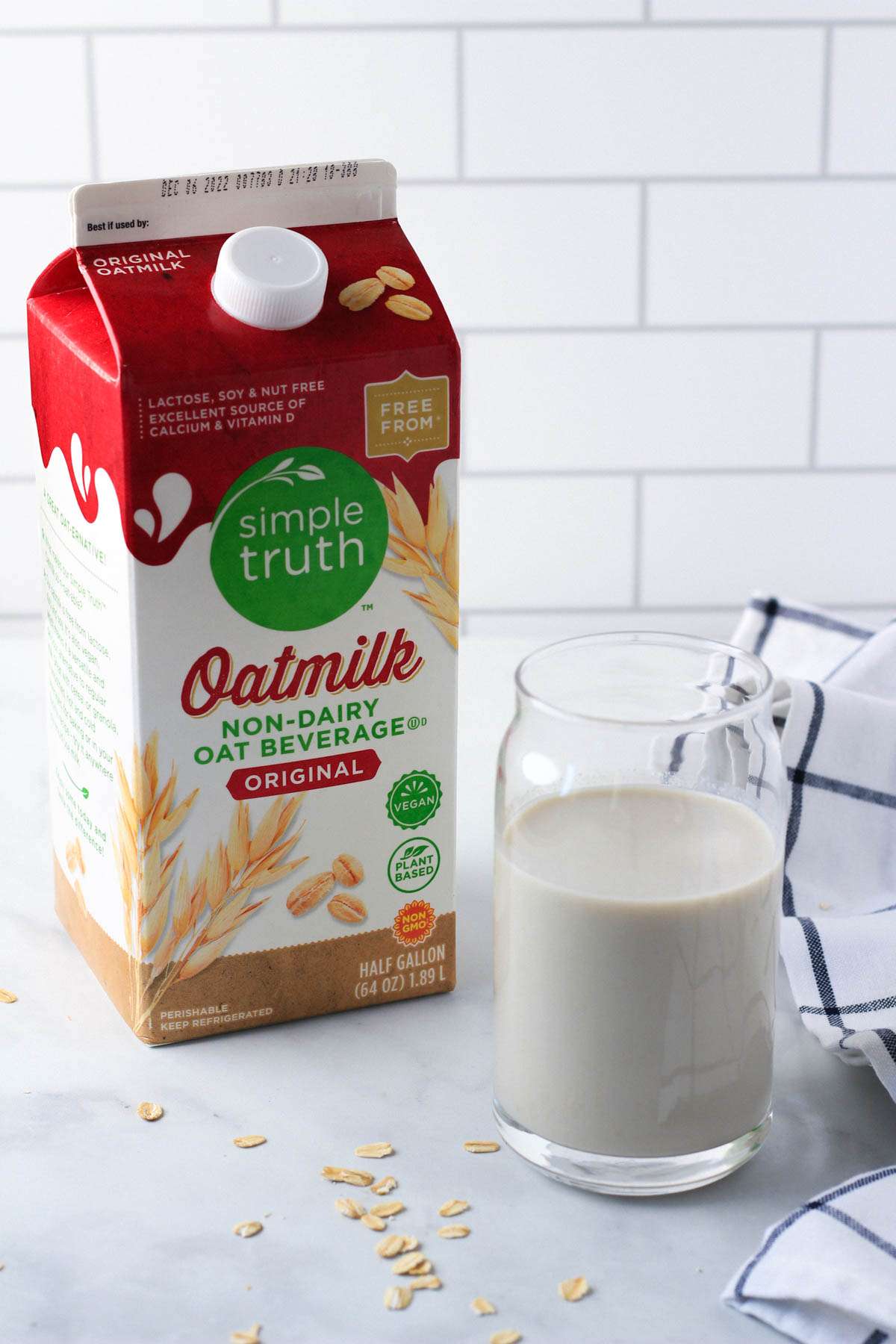 A carton of oat milk with a glass of oat milk to the right.