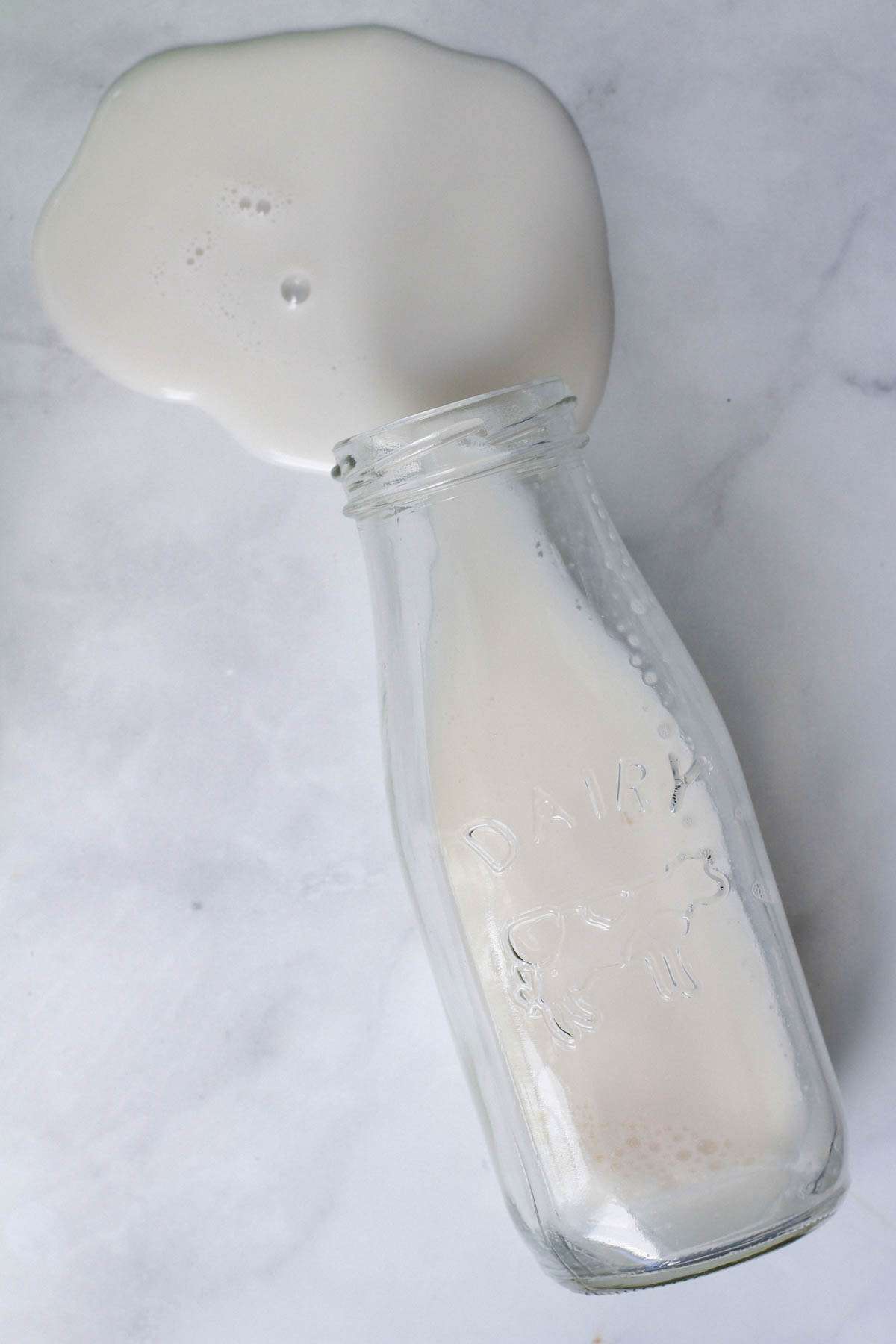 A glass of milk spilled on a white counter.