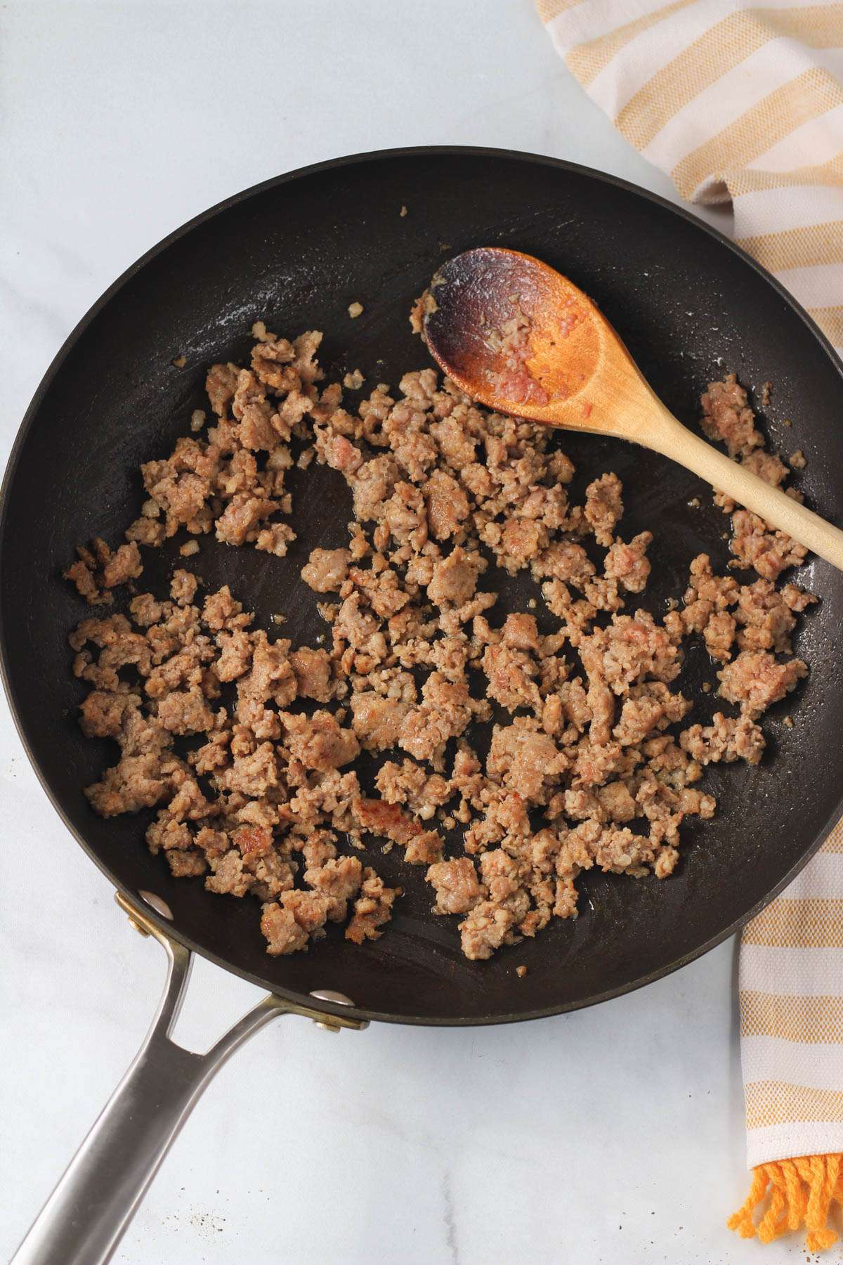 A non-stick skillet with a wooden spoon and cooked breakfast sausage.