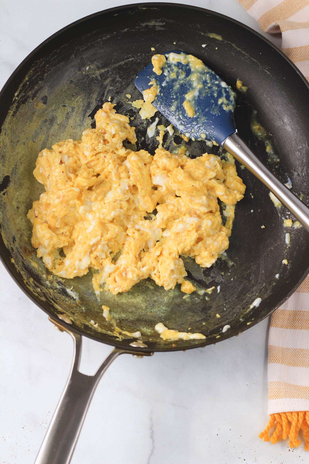 A non-stick skillet with a blue and silver spatula and cooked scrambled eggs.