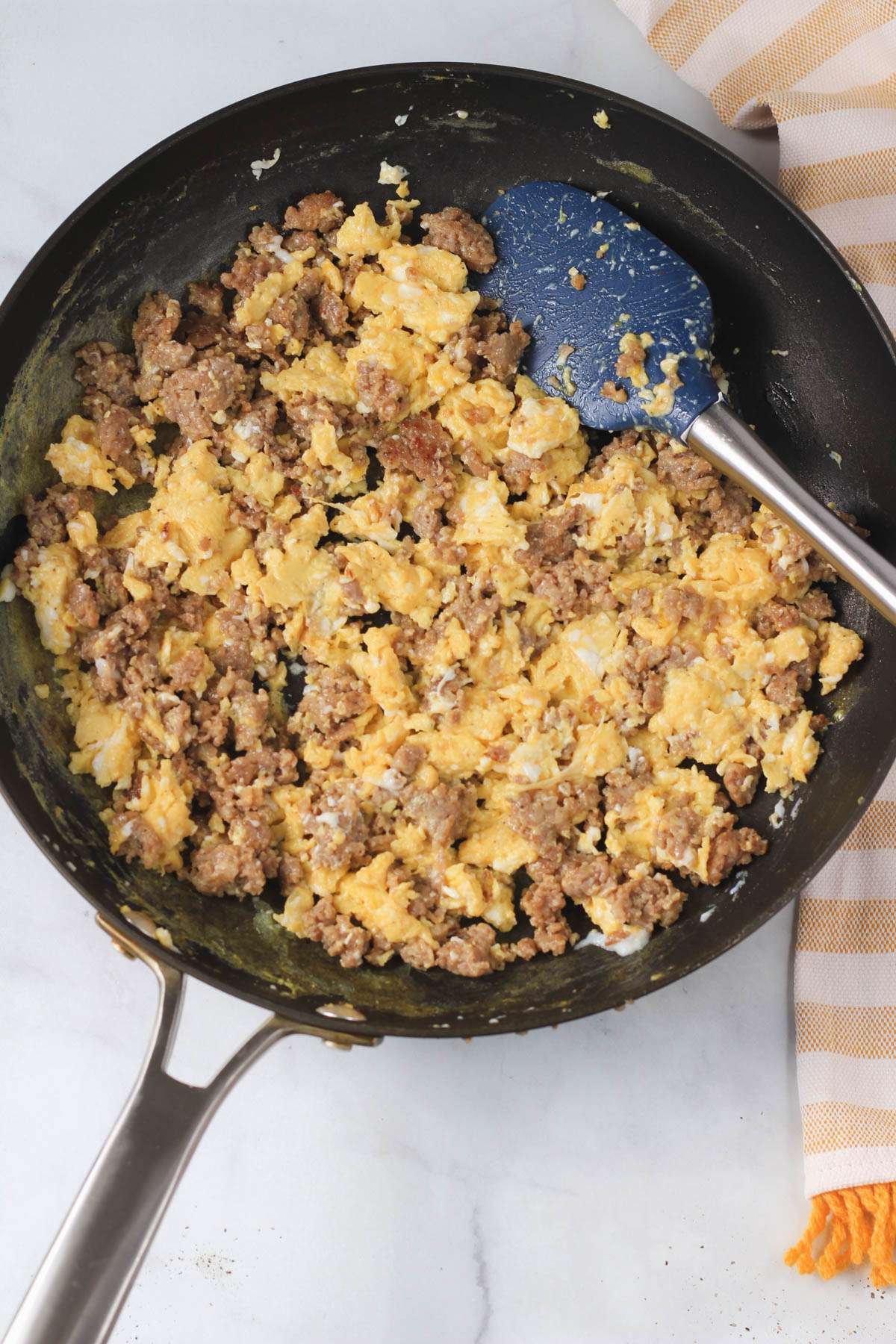 A non-stick skillet with scrambled eggs and sausage mixed together.