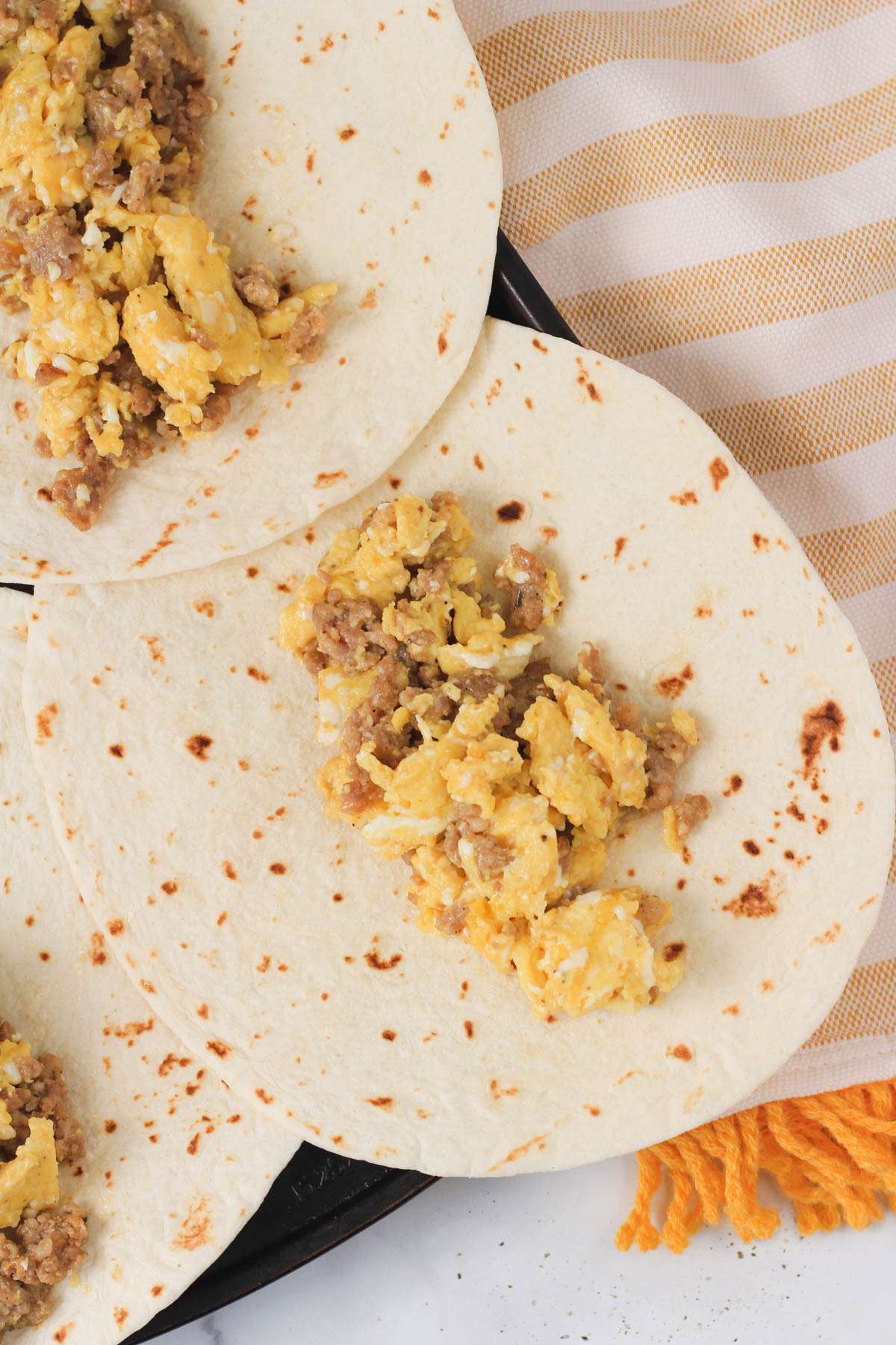 A flour tortilla with a scoop of sausage and egg mixture.