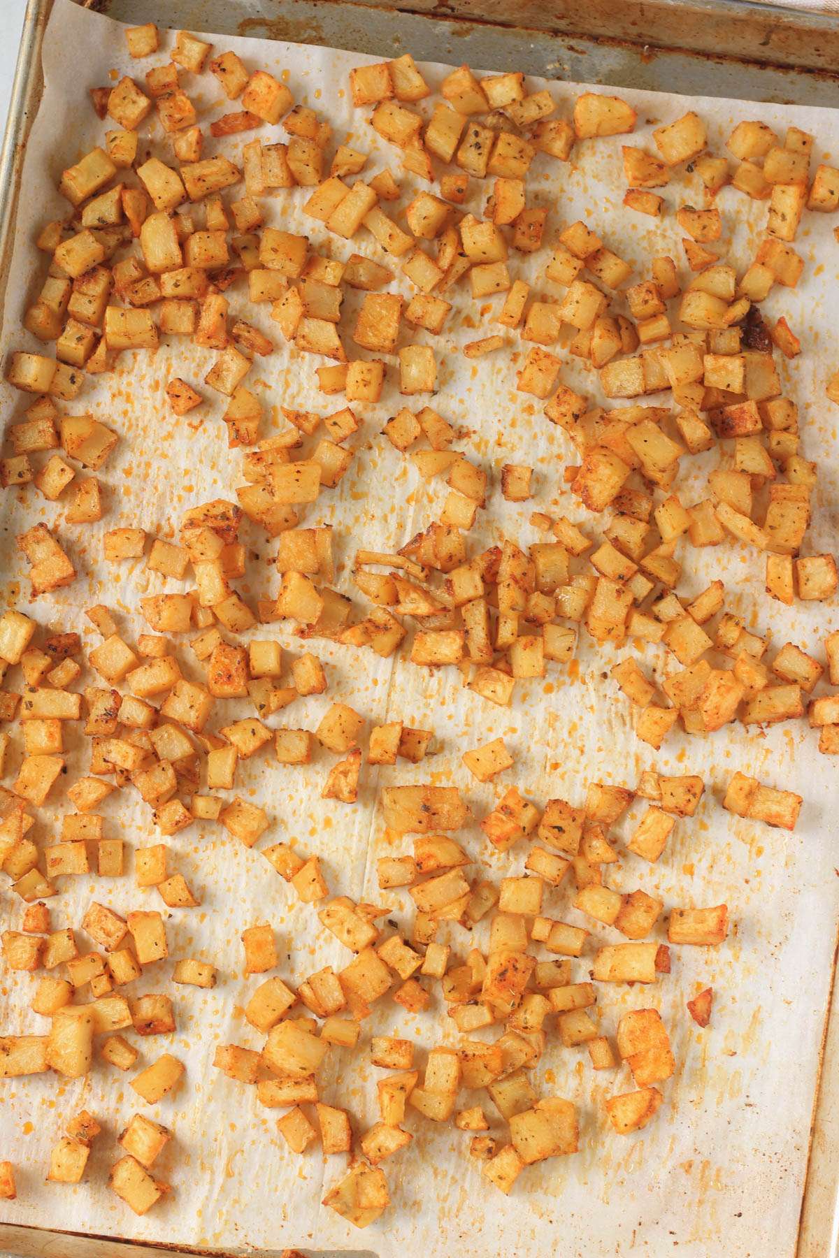 A parchment paper lined baking sheet with roasted breakfast potatoes after they have been cooked.