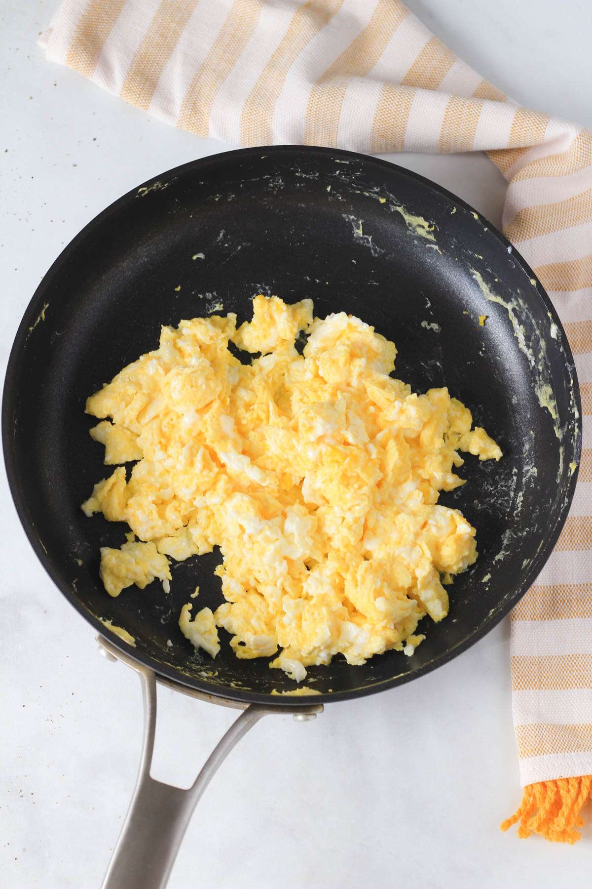 A non-stick skillet on a white counter with cooked scrambled eggs.