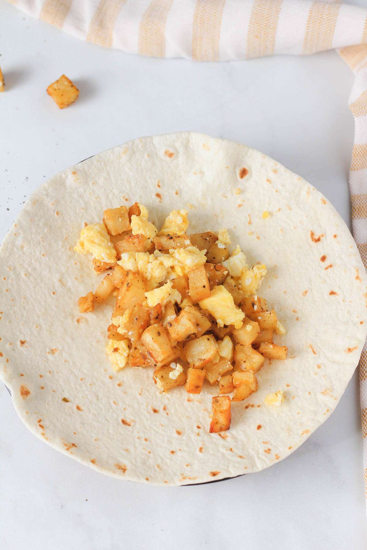 A flour tortilla filled with potato and egg before being wrapped.