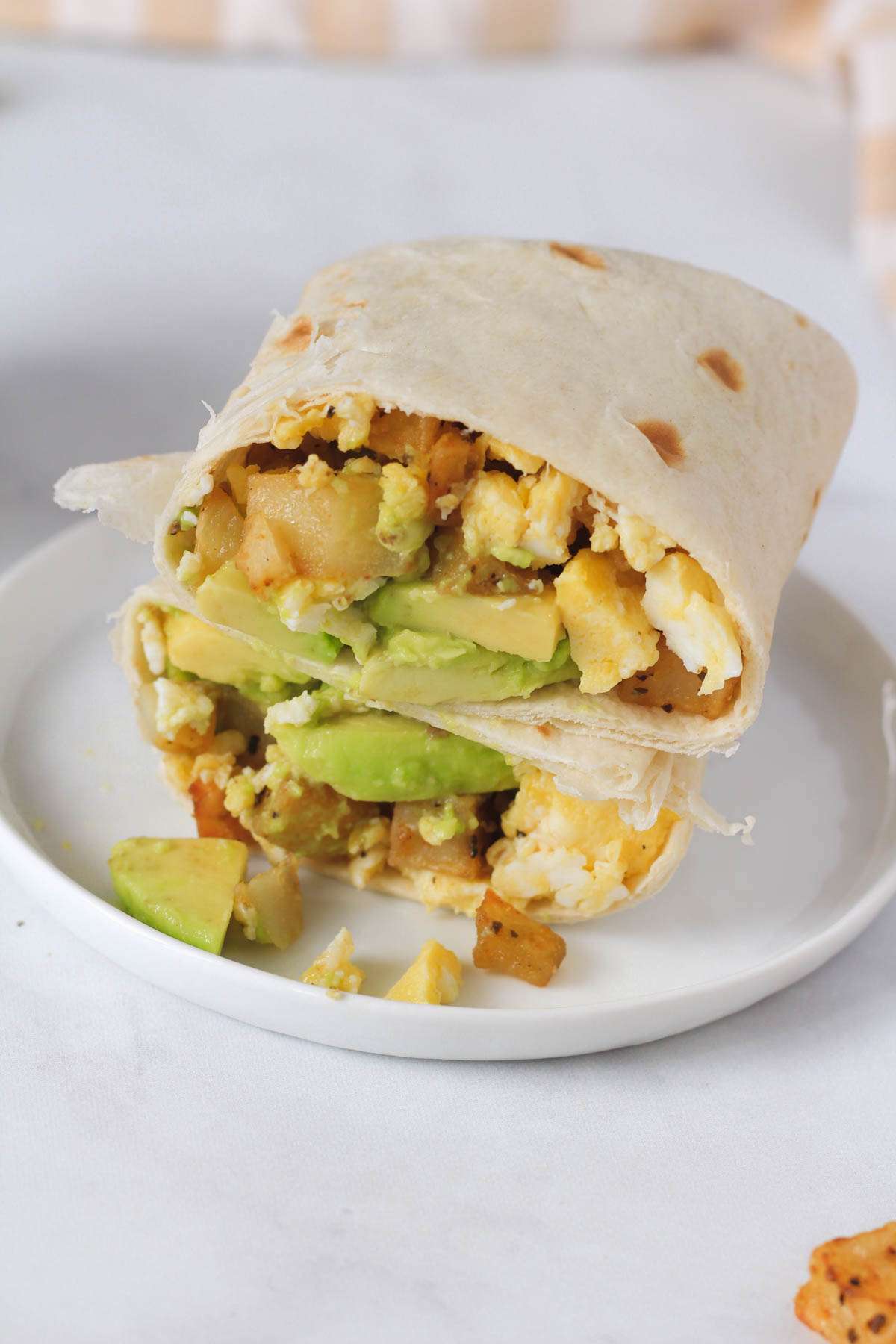 A white plate with a sliced breakfast burrito filled with potato, egg, and avocado.