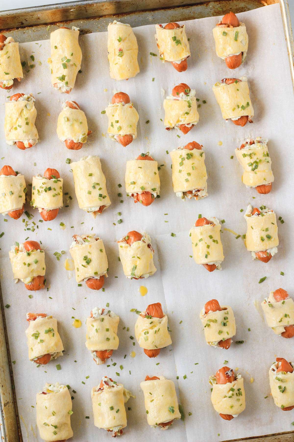 A parchment paper lined baking sheet with dairy-free jalapeño popper pigs in a blanket before baking.