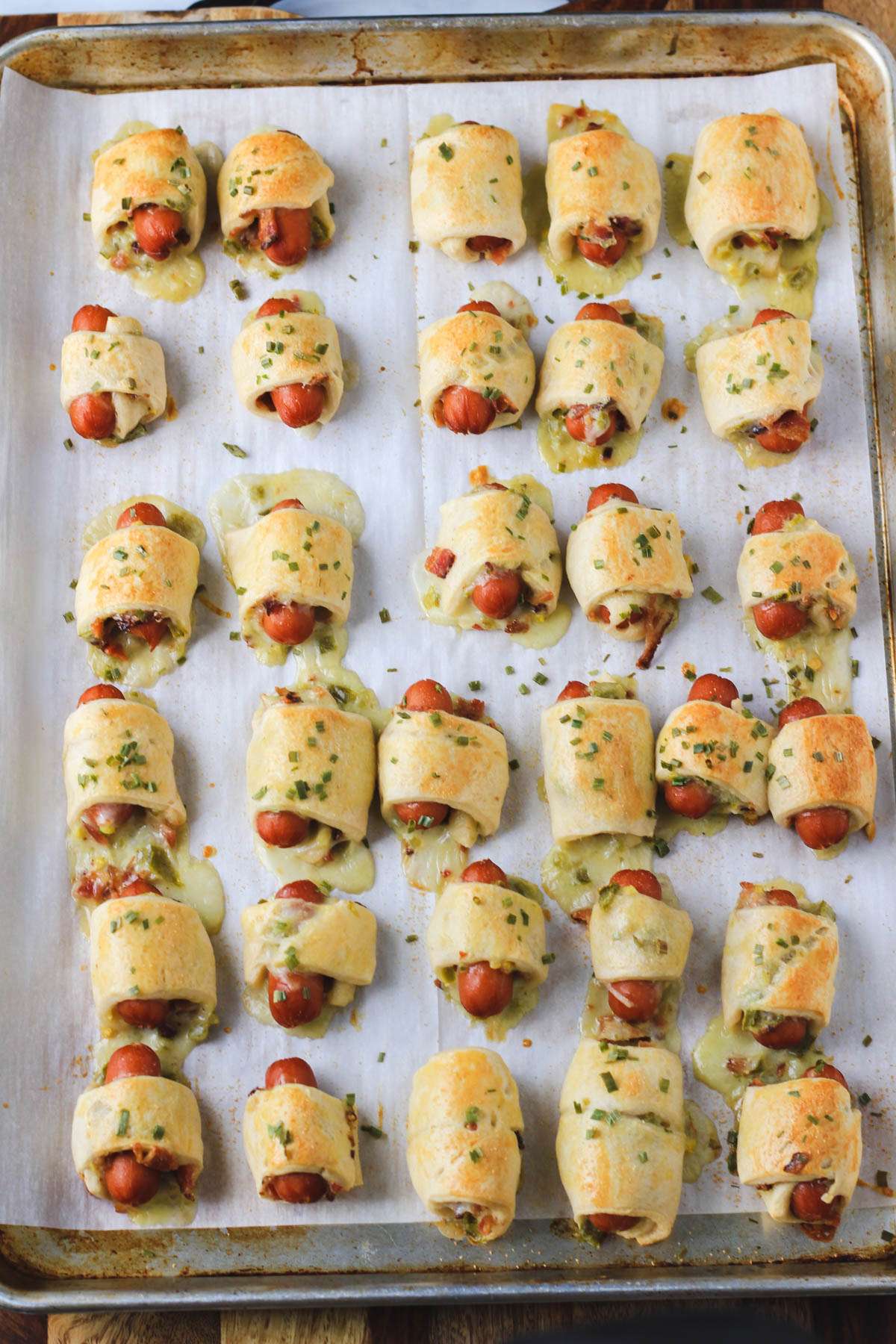 A parchment paper lined baking sheet with dairy-free jalapeño popper pigs in a blanket after baking.