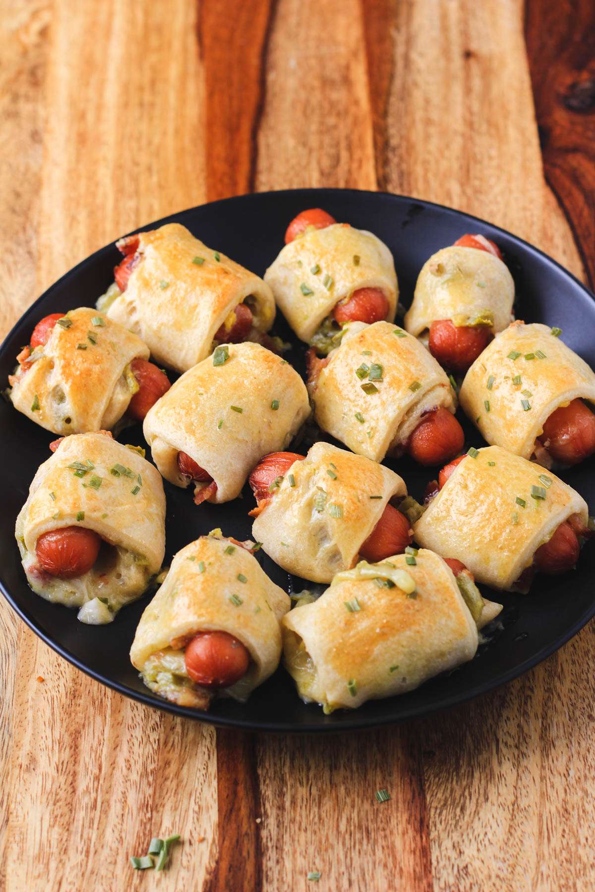 A black plate filled with pigs in a blanket on a wooden counter.
