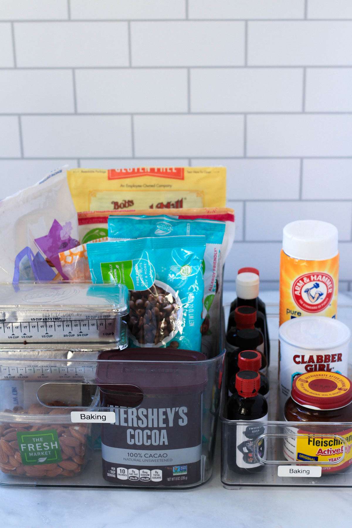 Baking ingredients in clear bins on a white counter.