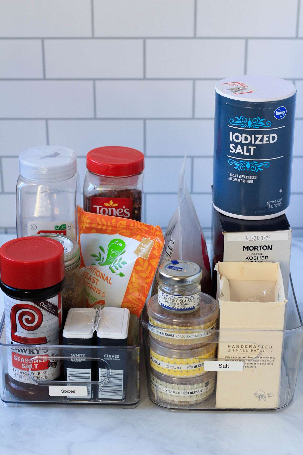 Spices and salts in plastic bins on a white counter.