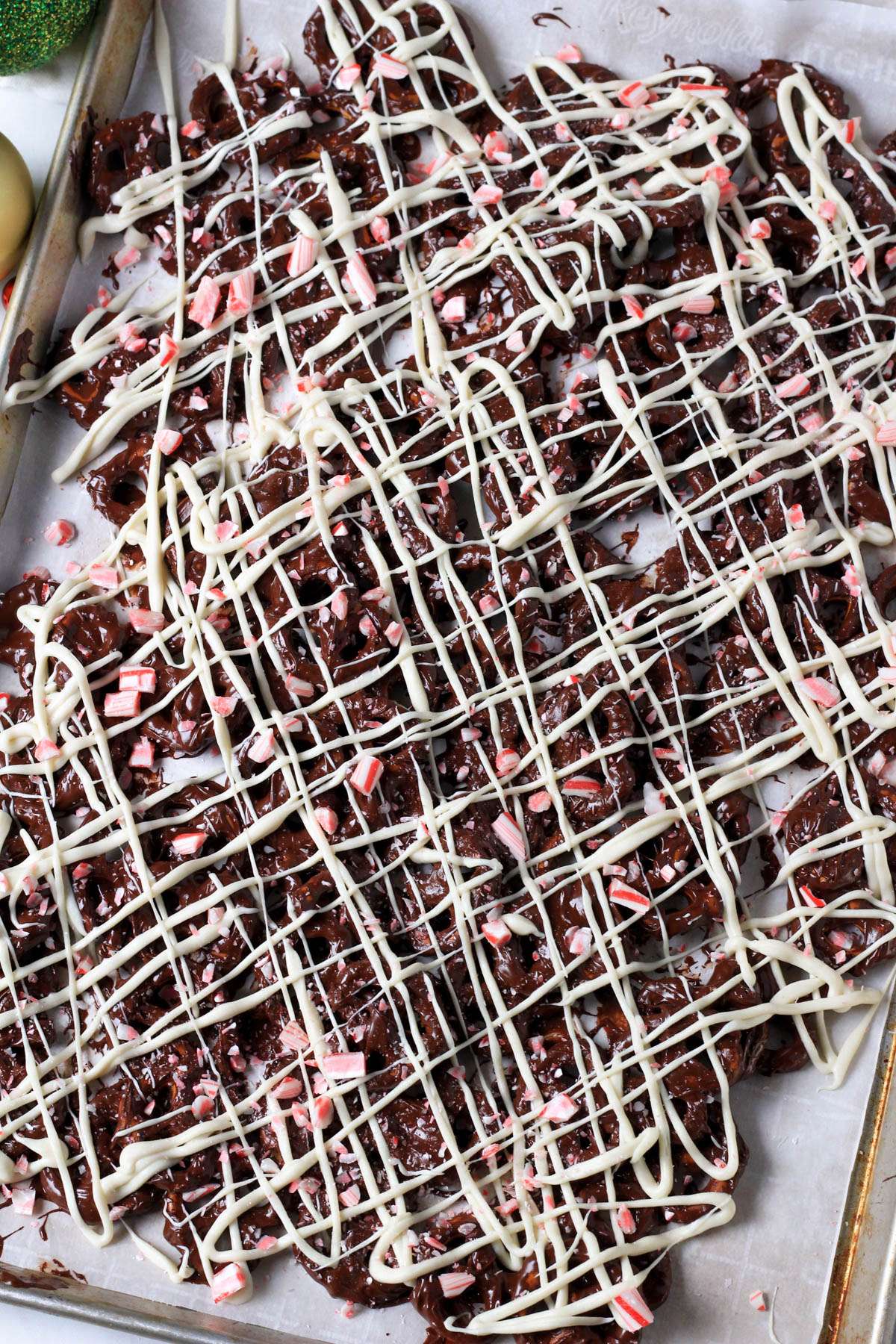 A parchment paper lined baking sheet with peppermint bark pretzels after drizzling white chocolate.