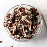 A close up of a glass bowl filled with peppermint bark pretzels topped with crushed candy cane.