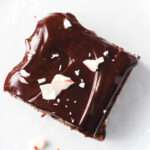 A slice of peppermint brownie with mint chocolate ganache sprinkled with crushed peppermint.