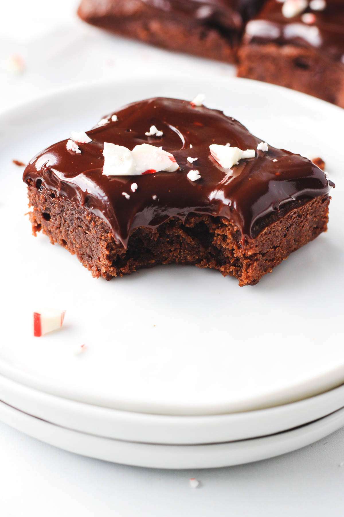 A stack of three white plates topped with one peppermint brownie with a bite taken out.