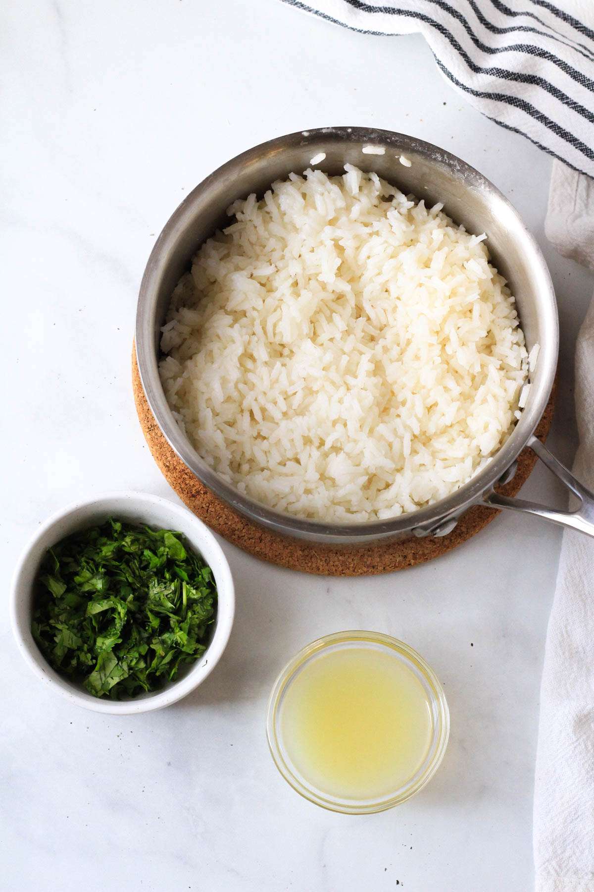 A sauce pan with cooked rice, a small bowl of chopped cilantro, and another small bowl of lime juice.
