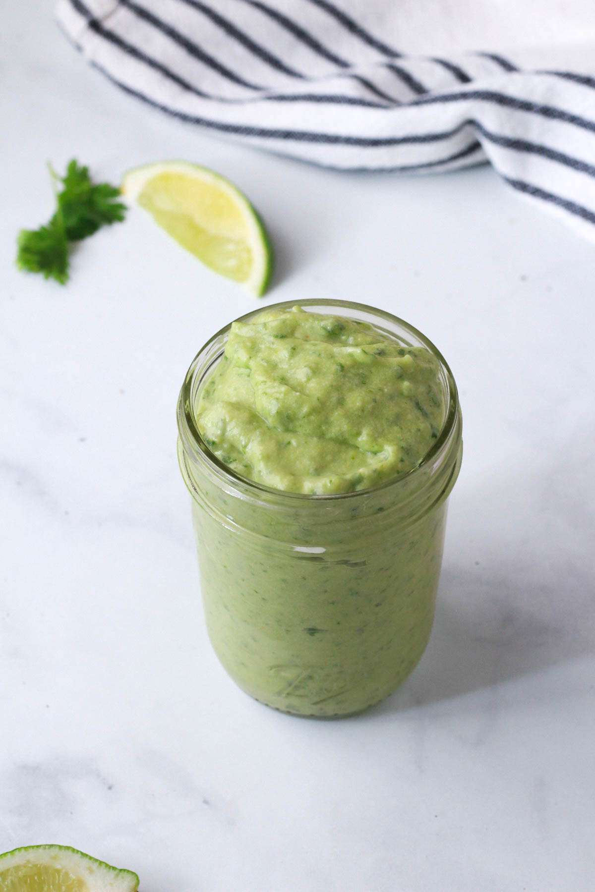 A mason jar with avocado cilantro dressing on a white counter.
