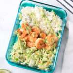 A close up of a glass pyrex with a serving of shrimp taco bowls topped with a zig zag of avocado cilantro dressing.