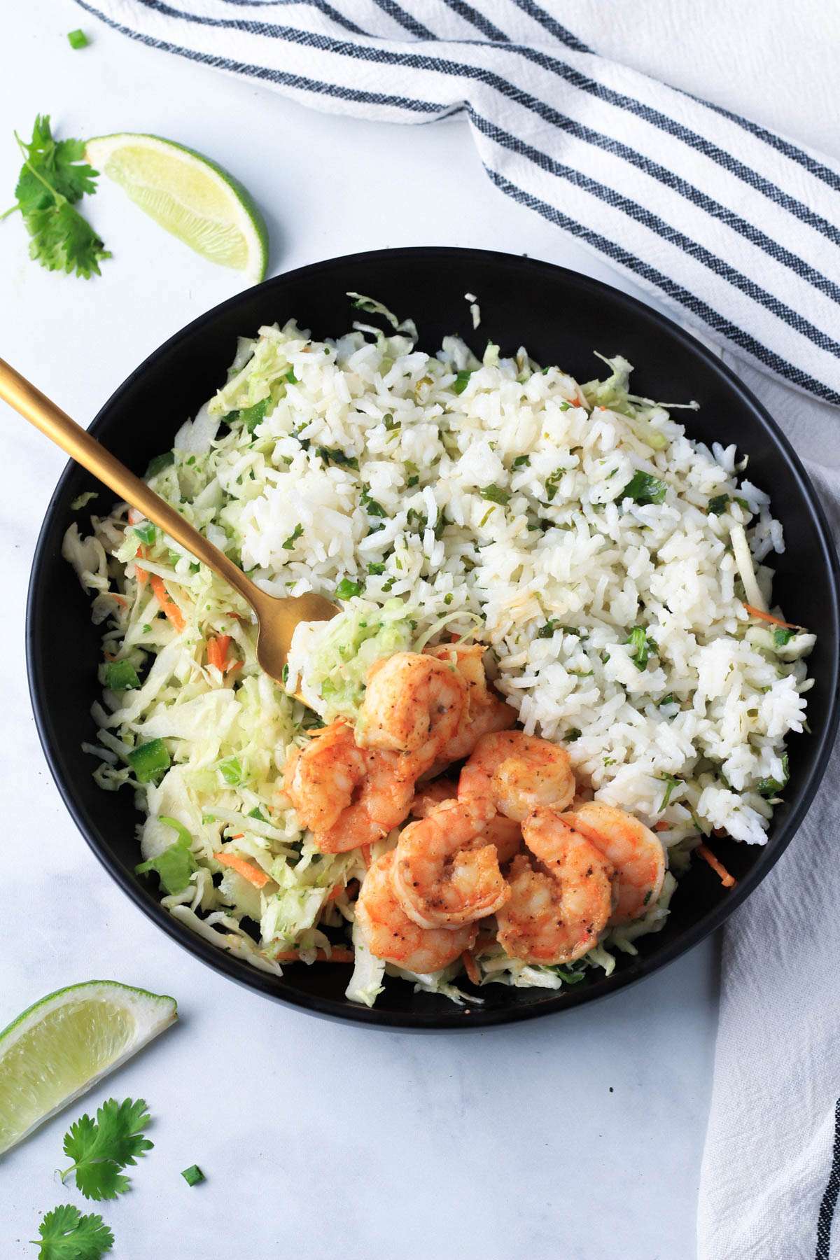 A black bowl with shrimp taco salad with a gold fork on the left side of the bowl.