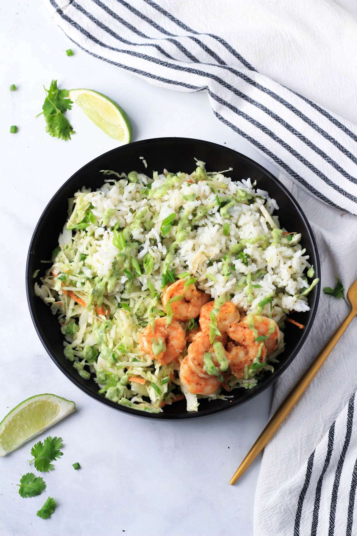 A black bowl on a white counter with shrimp taco salad filling the bowl and a gold fork to the right.