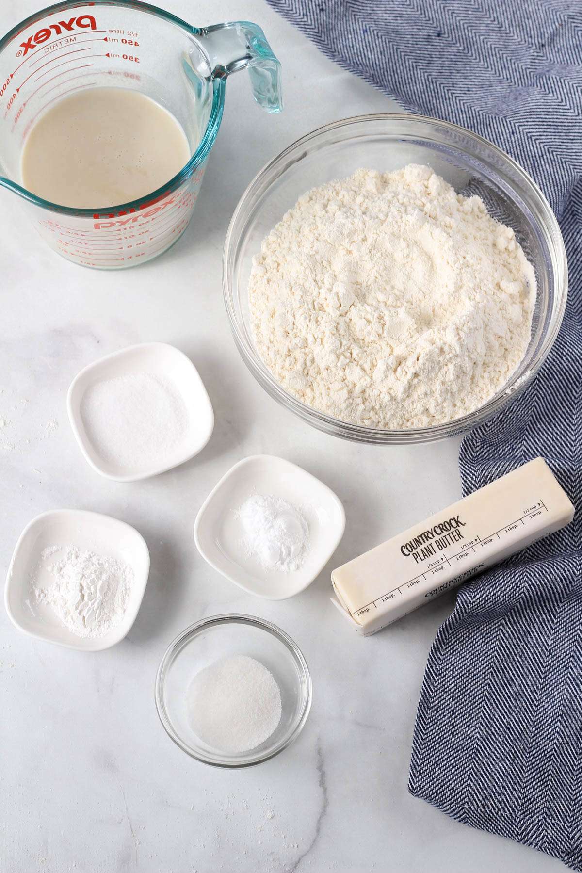 Ingredients for traditional buttermilk biscuits on a white counter with a blue dish towel.