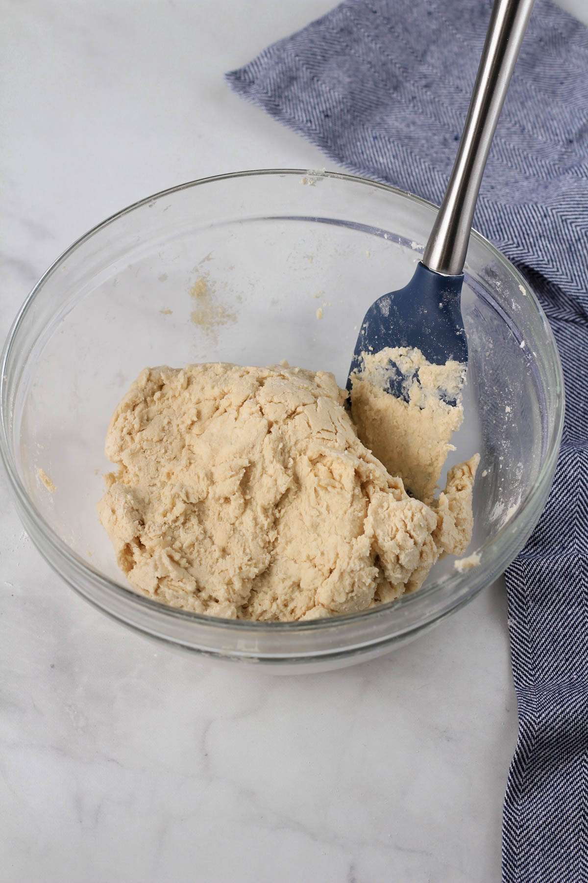 A glass mixing bowl after the buttermilk is added in with a blue and silver rubber spatula.