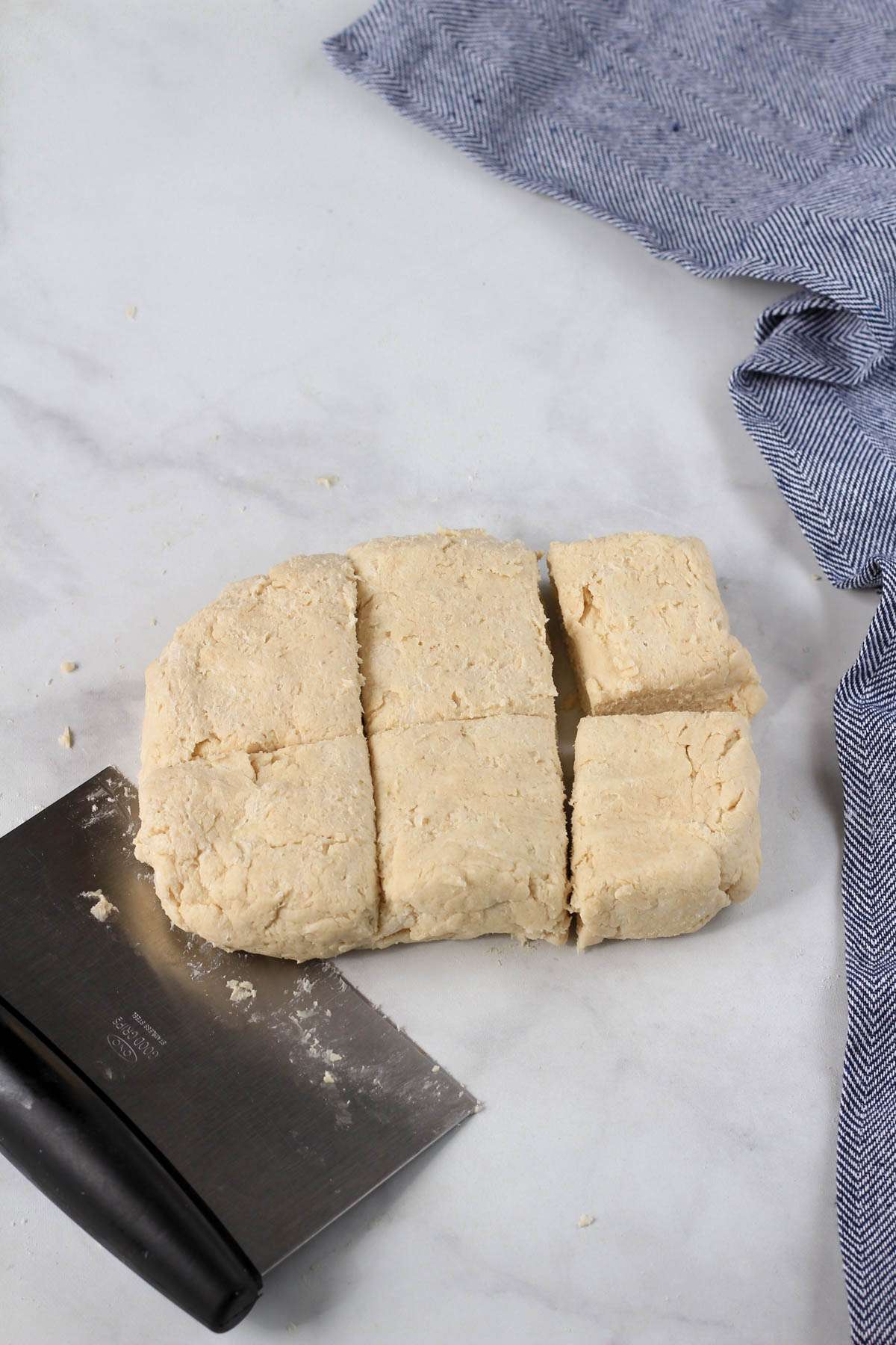 A white counter with a pastry scraper cutting the biscuit dough into squares.