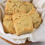 A close up of baked buttermilk biscuits in a white towel lined basket.
