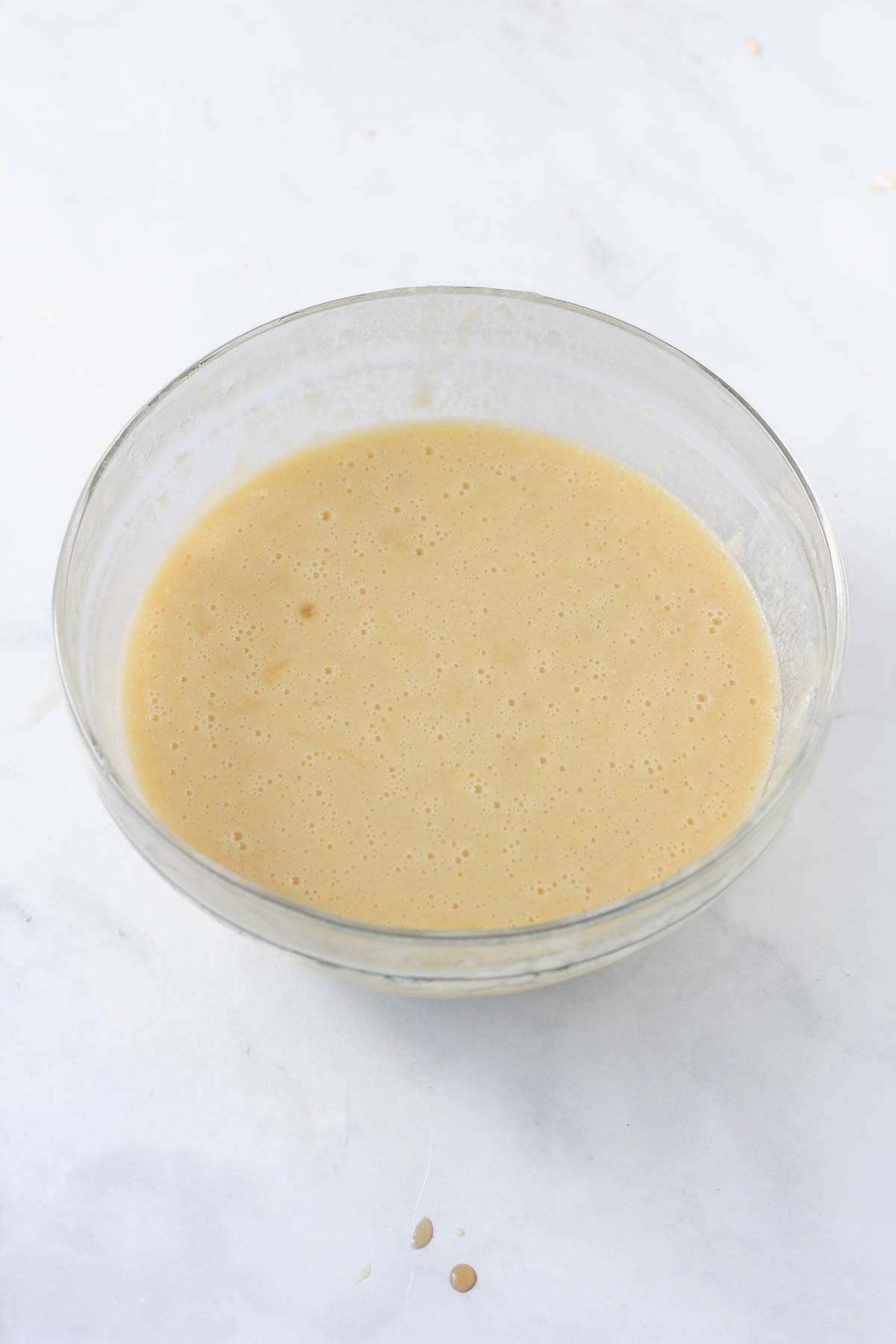 A glass mixing bowl with wet ingredients for banana baked oatmeal mixed together.