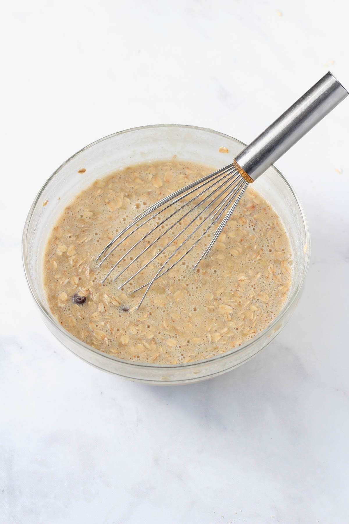 All ingredients for banana baked oatmeal with chocolate chips in a large glass mixing bowl with a whisk.