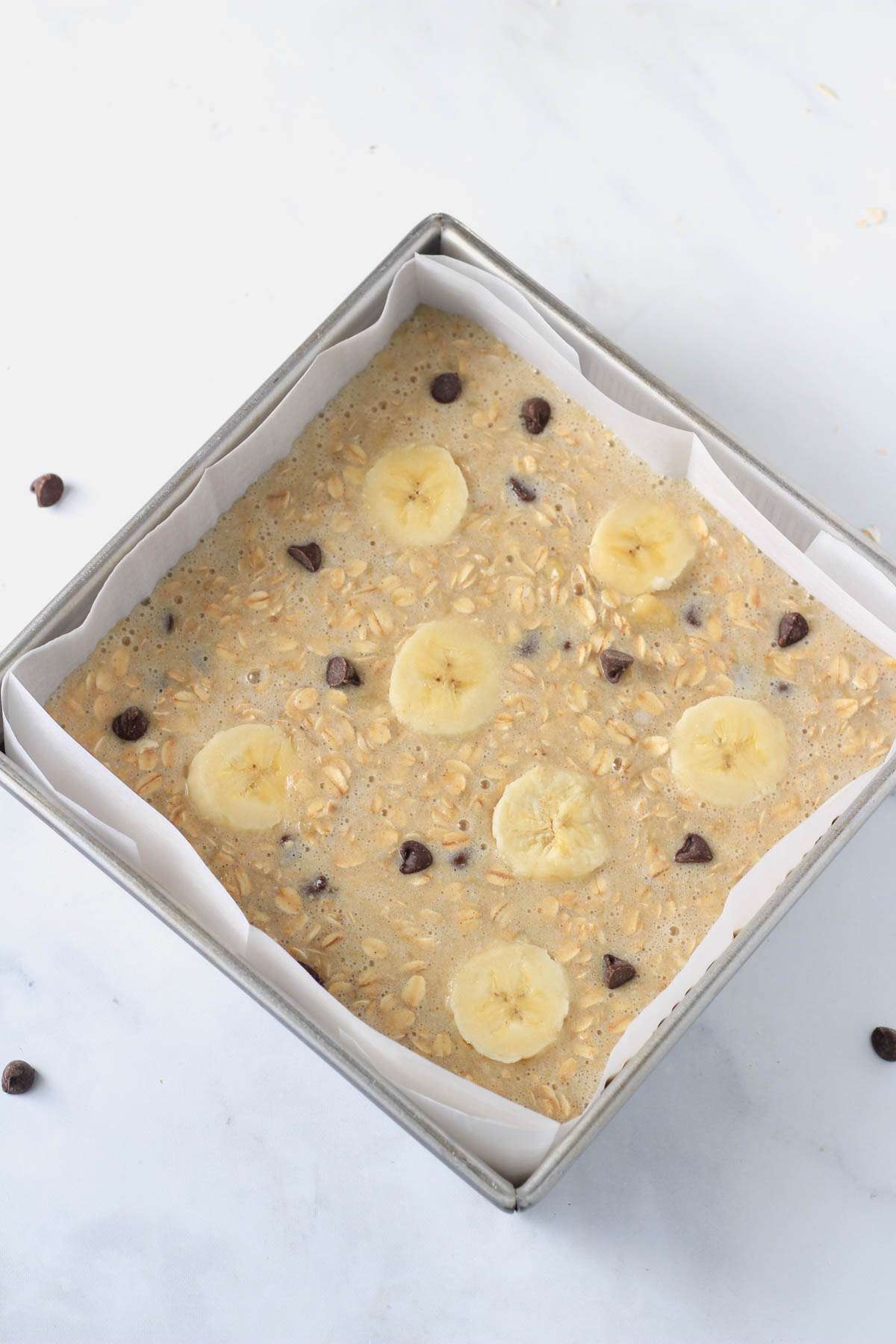 A square baking pan with banana baked oatmeal bars before baking.