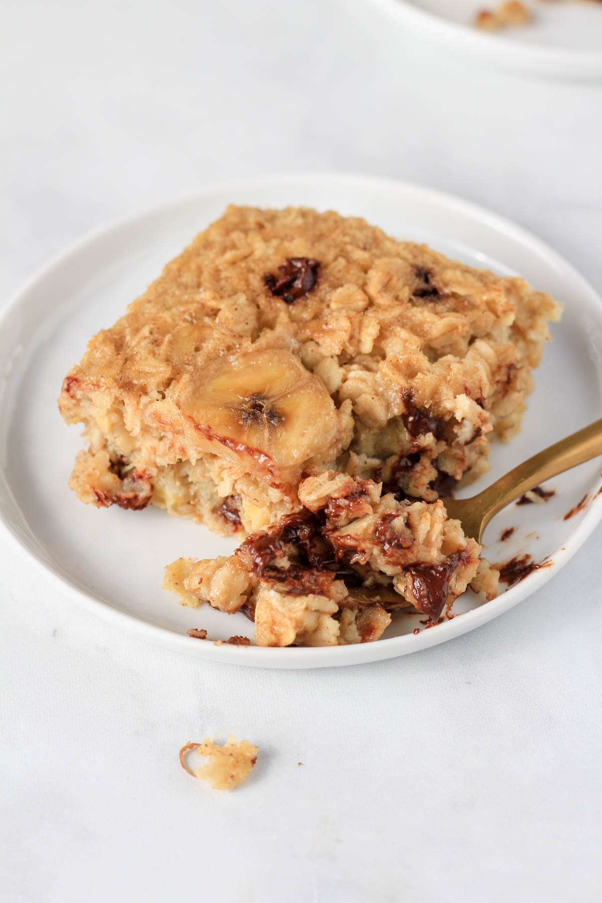A small white plate with a banana oatmeal bar and a gold fork with a bite out.