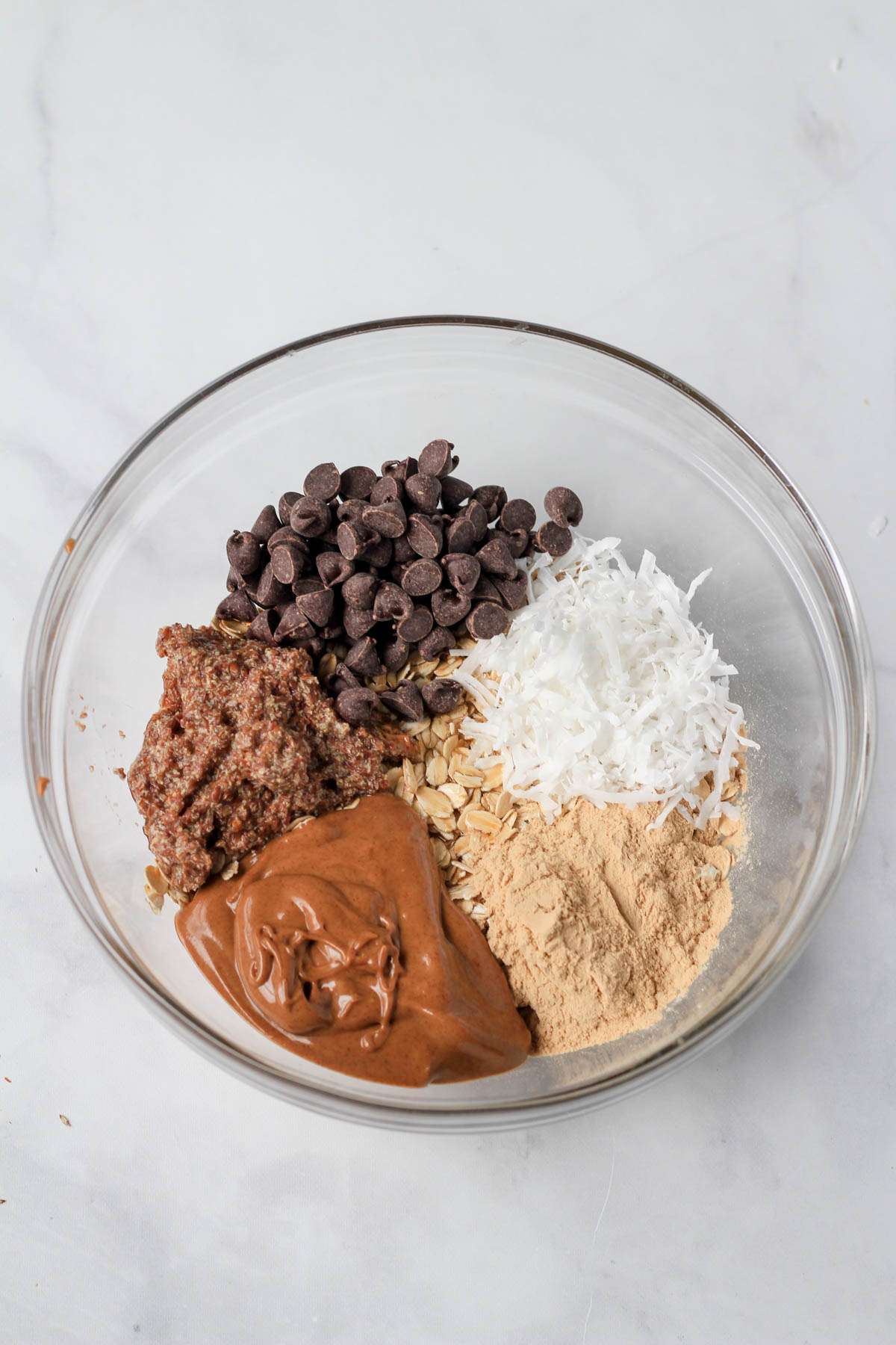 A clear glass bowl with all of the ingredients for almond joy lactation bites before mixing together.