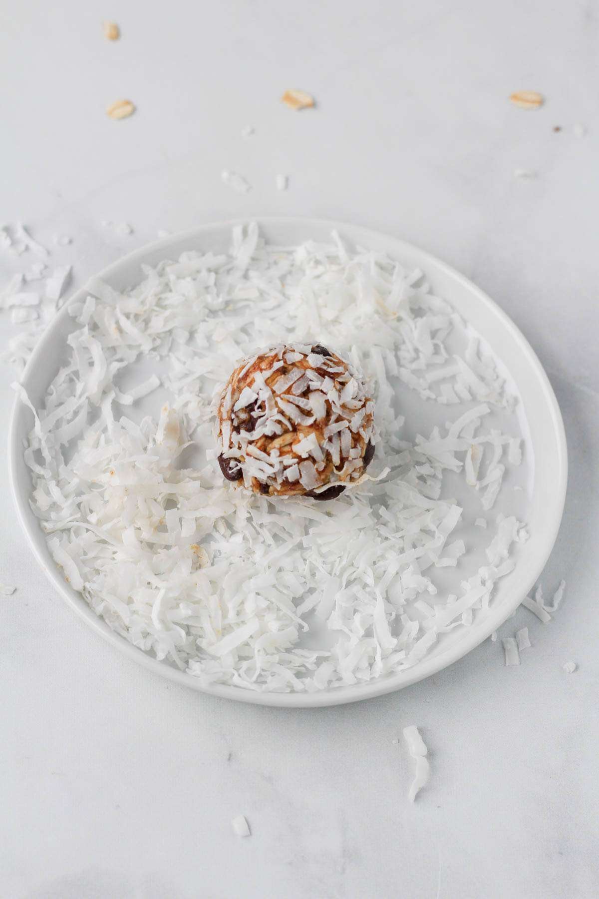 A small white plate with shredded coconut and a small lactation bite coated in the coconut.