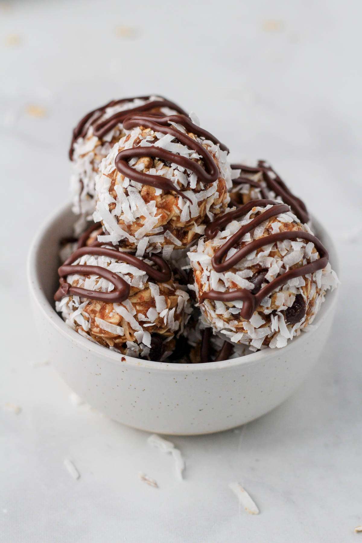 A small white bowl on a white counter with almond joy lactation bites drizzled with melted chocolate.