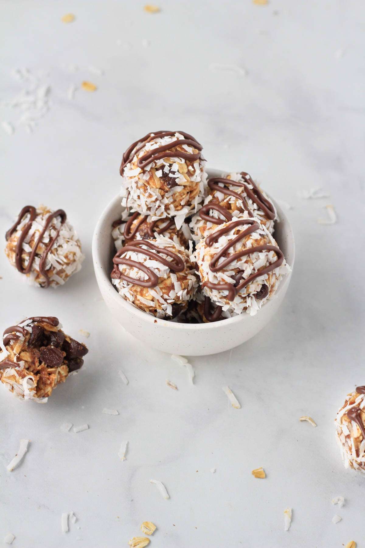 A white counter with a small white bowl filled with lactation bites and a few almond joy bites on the counter around the bowl.