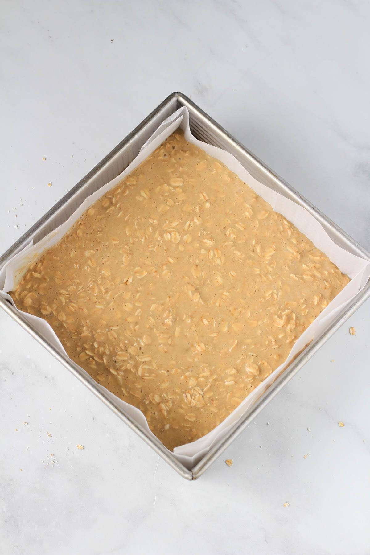 A parchment paper lined baking dish with the unbaked peanut butter oatmeal batter.