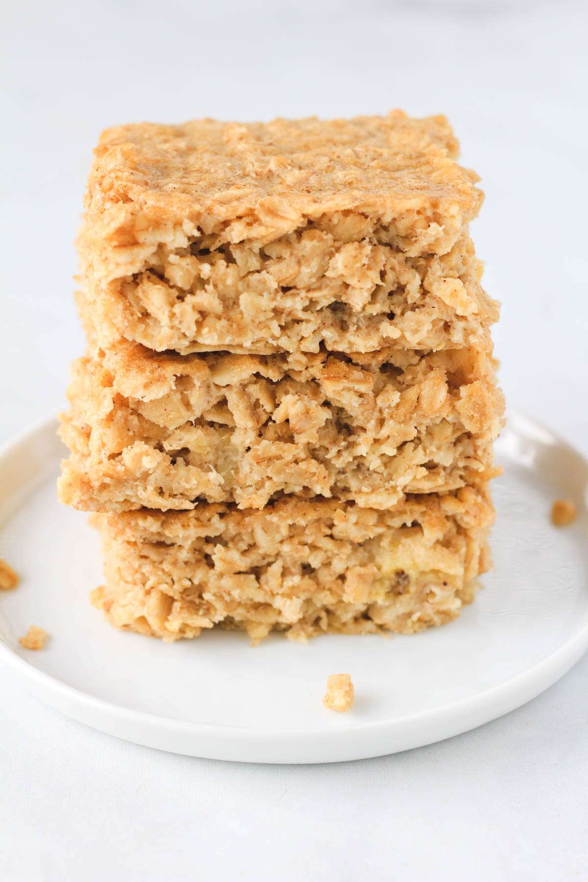 A stack of three peanut butter baked oatmeal squares on a white plate on a white counter.